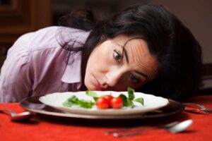 Donna a dieta che guarda sconfortata un piatto d'insalata