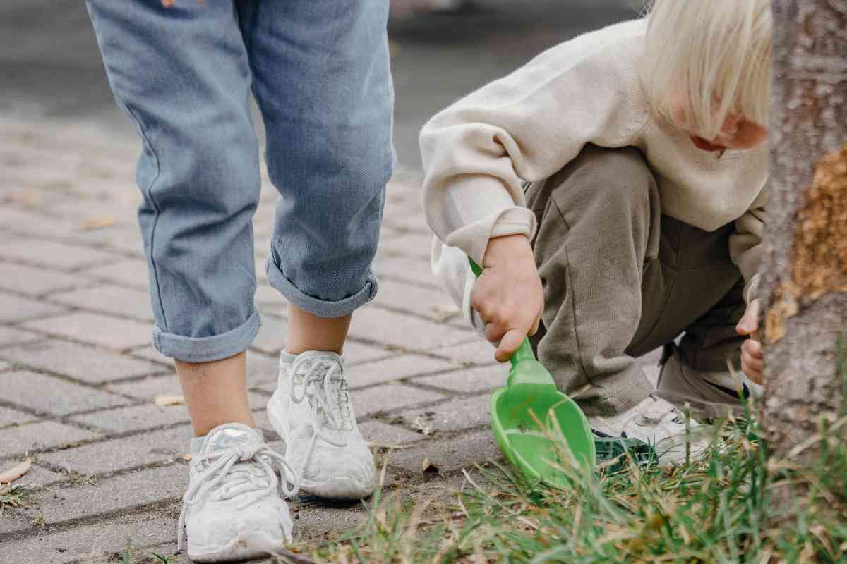 Un bambino biondo che scava con una paletta in un giardino