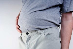 Uomo con maglietta grigia che si tocca la pancia gonfia in primo piano