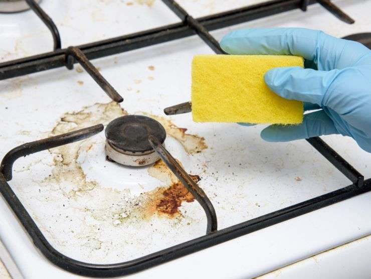 fornello incrostato e mano con spugna che per pulire