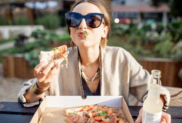 donna con gli occhiali da sole che mangia una pizza