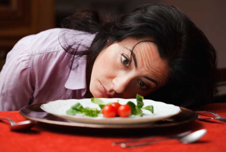 ragazza con la testa sul tavolo e piatto davanti